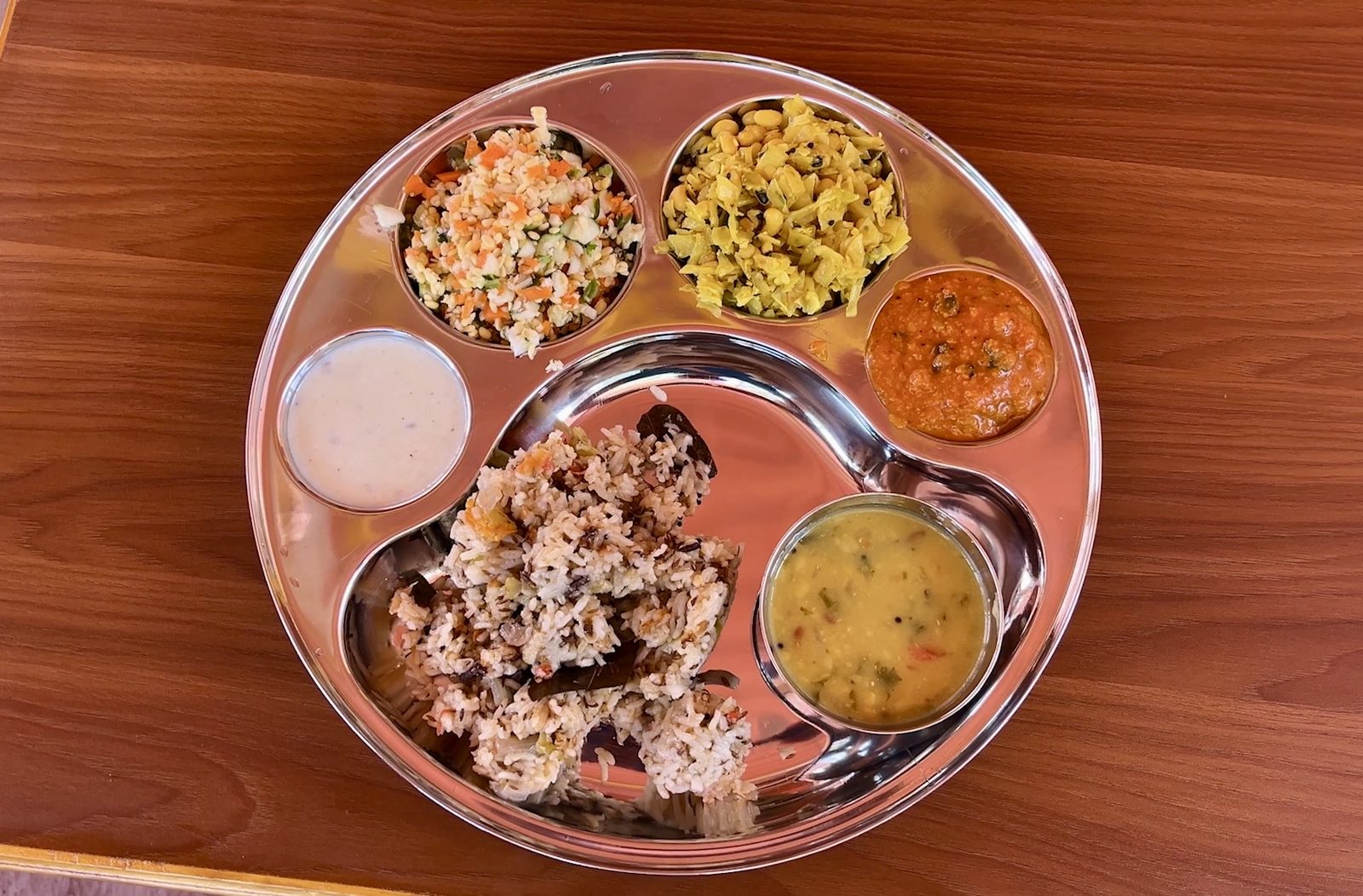 A vegetarian thali of rice, dal, sabzi, salad, chutney and curd served on a steel plate
