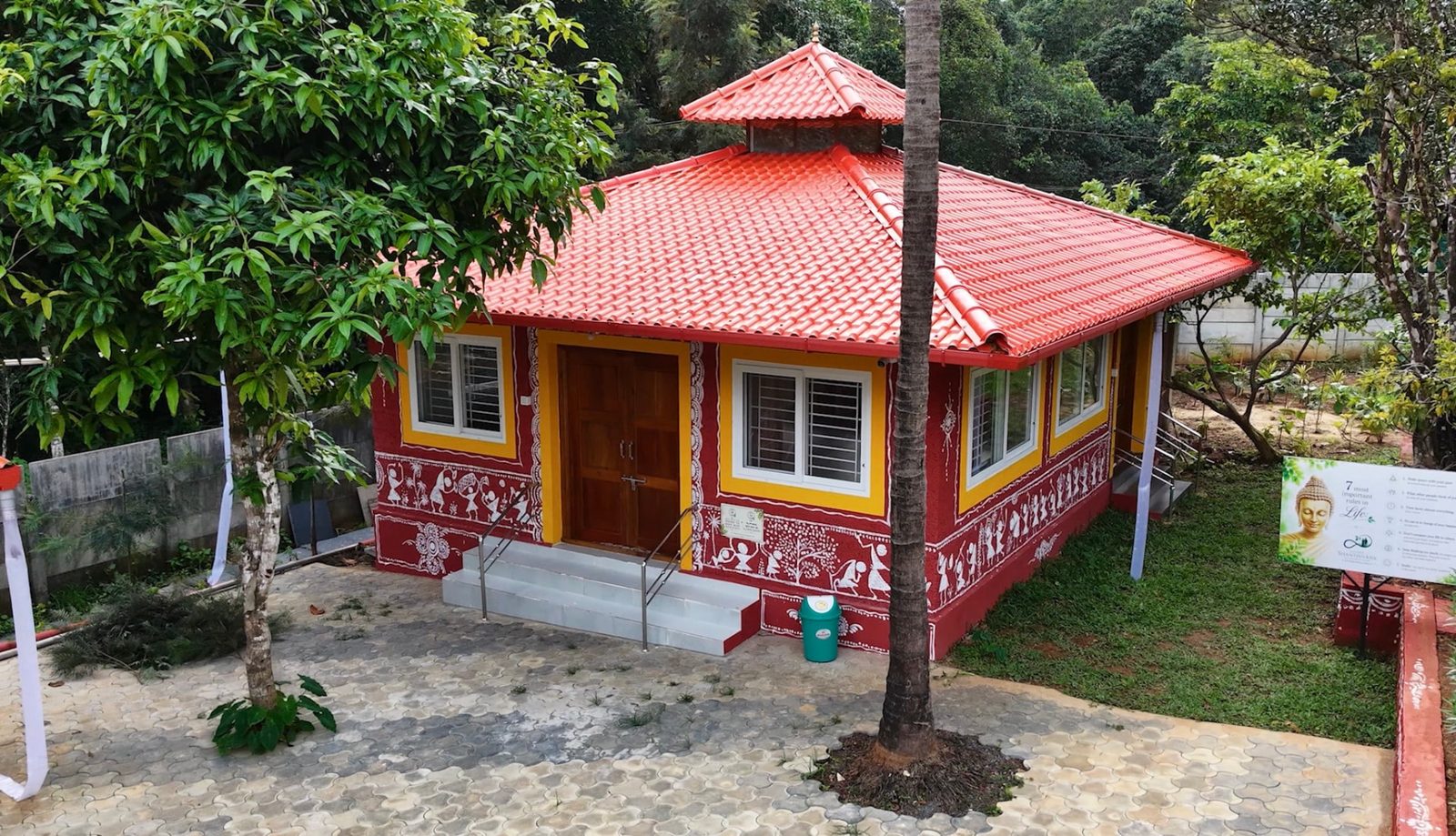 The red and yellow meditation cottage with a tiled pyramid roof surrounded by trees